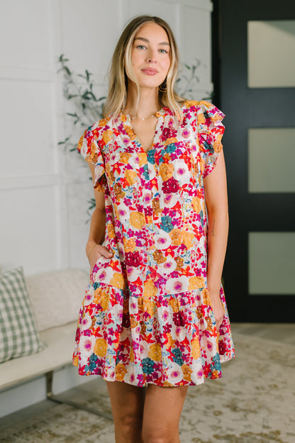 Woman wearing a colorful floral dress in a room with a couch and plant.