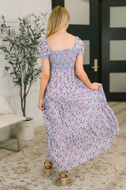 Woman in a floral dress walking in a room with a plant and door in the background