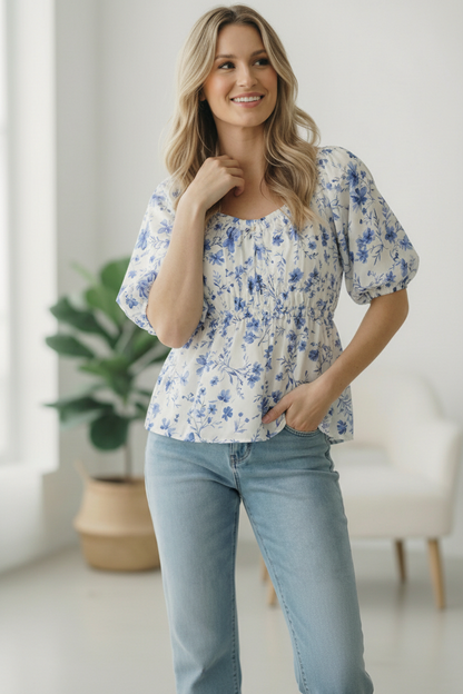 Woman wearing a floral blouse and light blue jeans indoors.