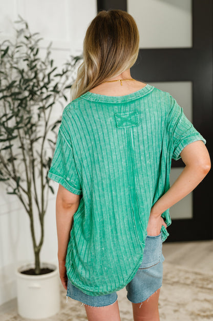 Woman wearing a green textured top and denim shorts in an indoor setting.
