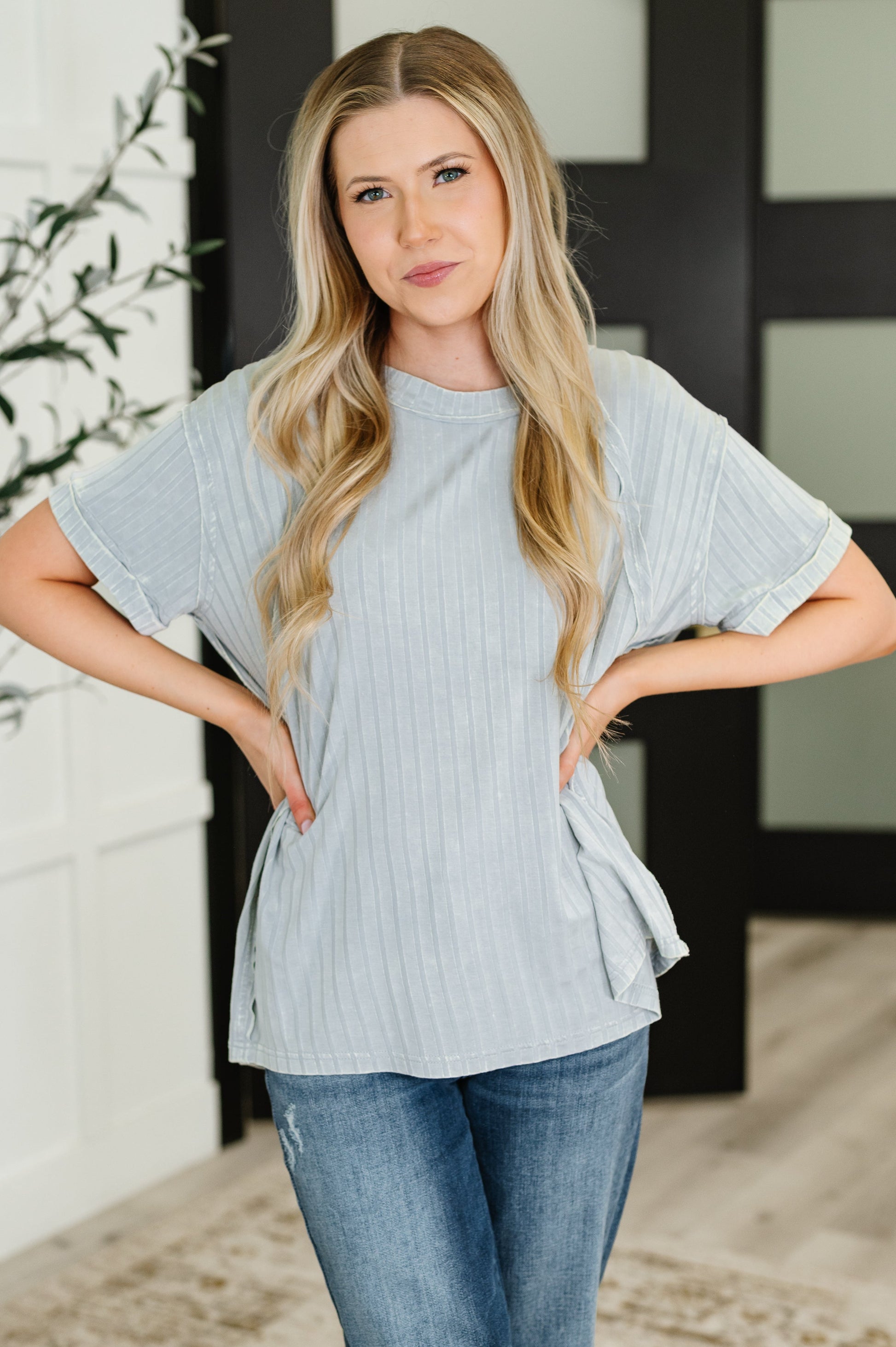 Woman wearing a light blue ribbed top and jeans indoors.