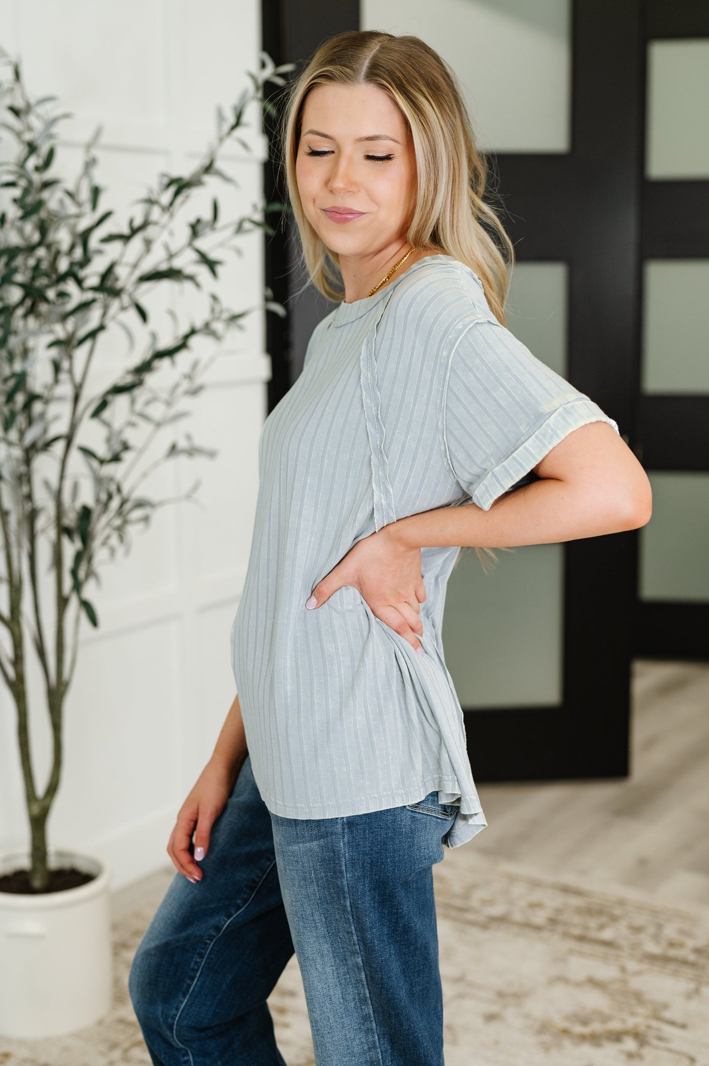Woman wearing a light blue ribbed sweater and jeans standing indoors.