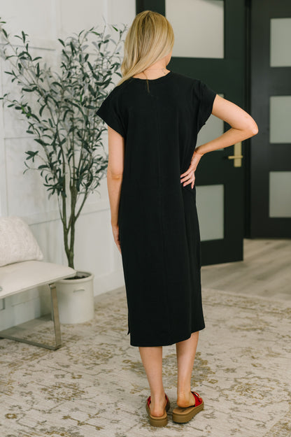 Woman wearing a black dress standing in a room with a plant and door in the background