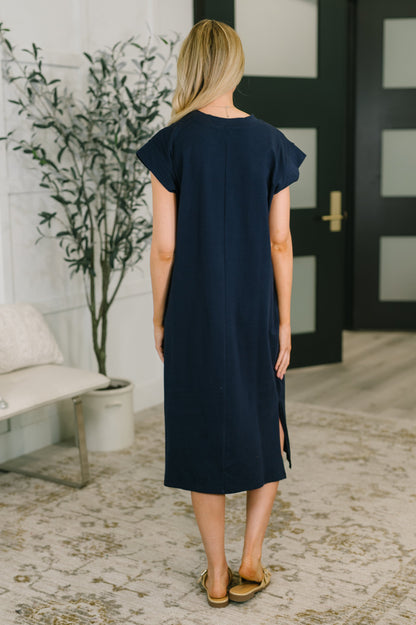 Woman wearing a navy blue dress in an indoor setting with a plant and door in the background.