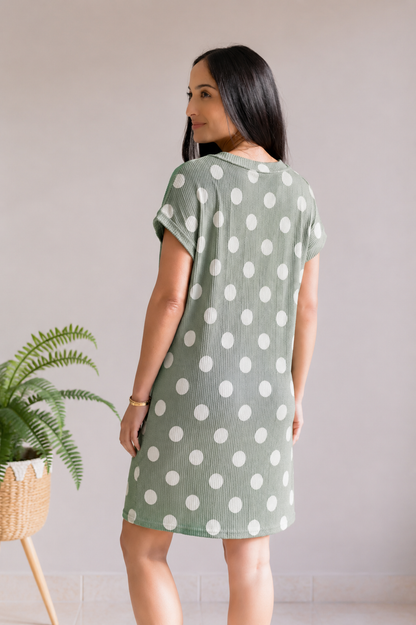 Woman wearing a green dress with white polka dots, standing indoors.