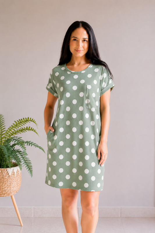 Woman wearing a green polka dot dress standing in a minimalistic room with a plant.
