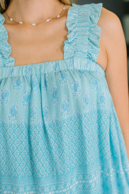 Close-up of a light blue dress with intricate patterns and ruffled straps.