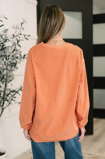 Person wearing an orange corded sweatshirt and blue jeans in a room with a plant and mirror.
