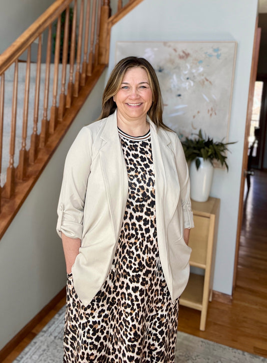 Woman in a leopard print dress and beige cardigan standing in a home interior.