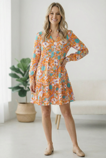 Woman wearing a floral dress in a bright room with a plant and chair.