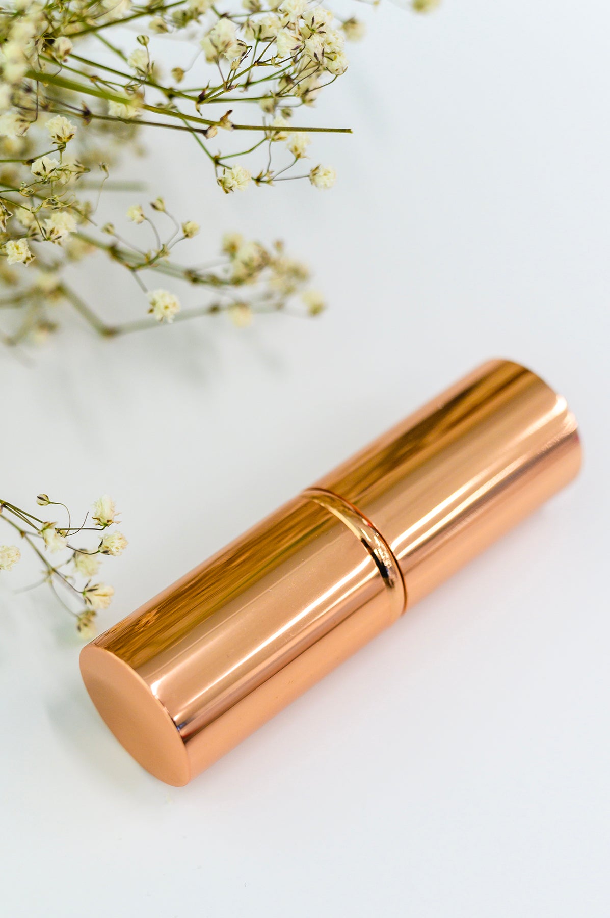 Rose gold lipstick on a light background with small white flowers