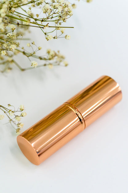 Rose gold lipstick on a light background with small white flowers