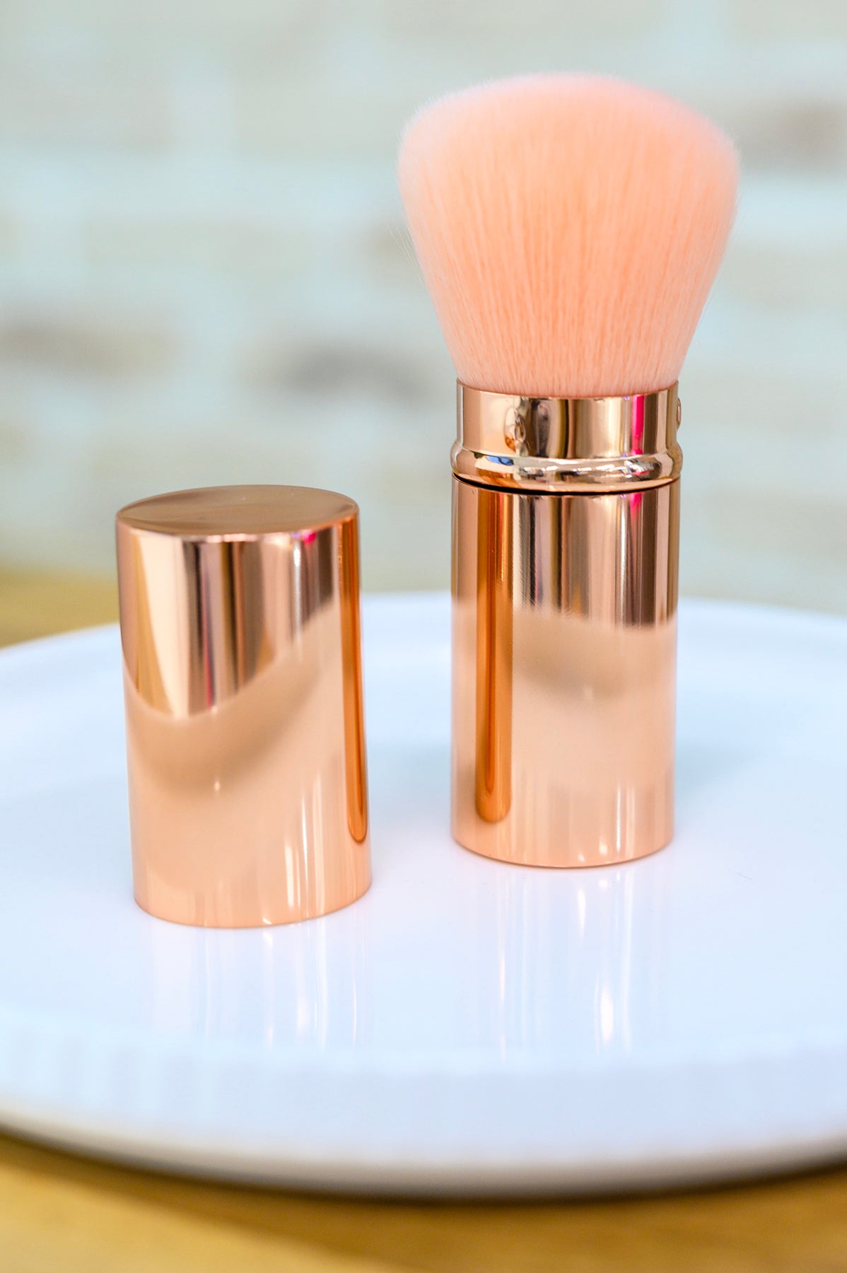 Rose gold makeup brush with a matching holder on a white surface.