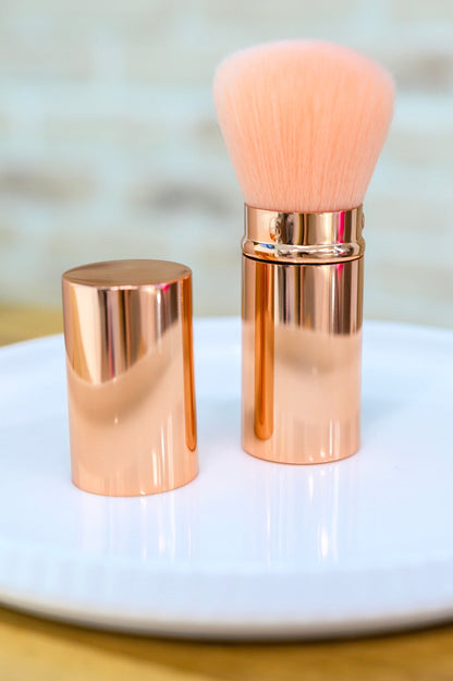 Rose gold makeup brush with a matching holder on a white surface.