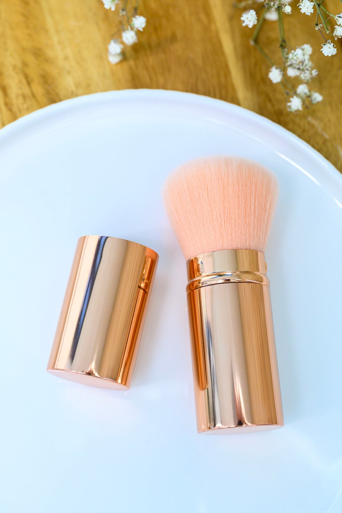 Makeup brush with rose gold casing on a white plate with a wooden background