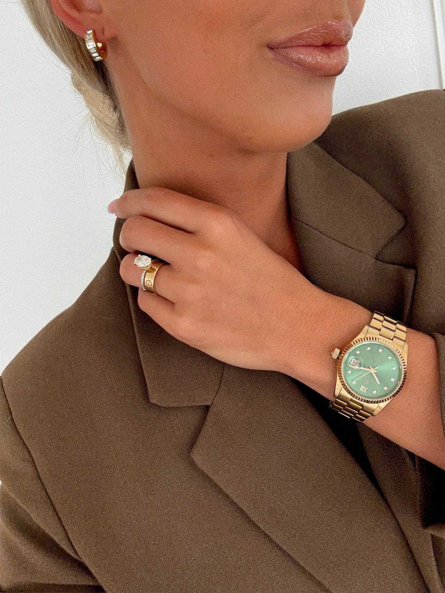 Woman wearing a gold watch and ring, adjusting her blazer collar.