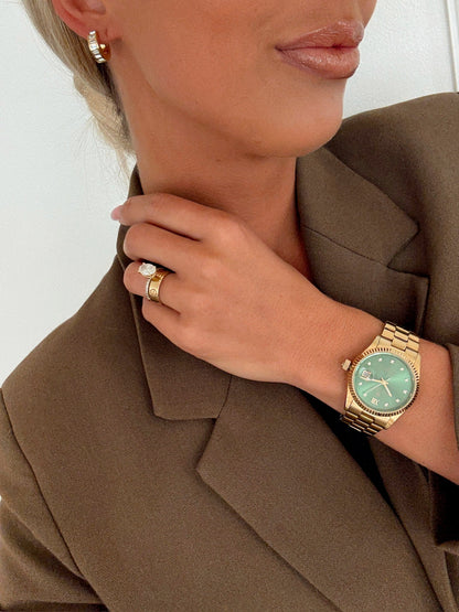 Woman wearing a gold watch and ring, adjusting her blazer collar.