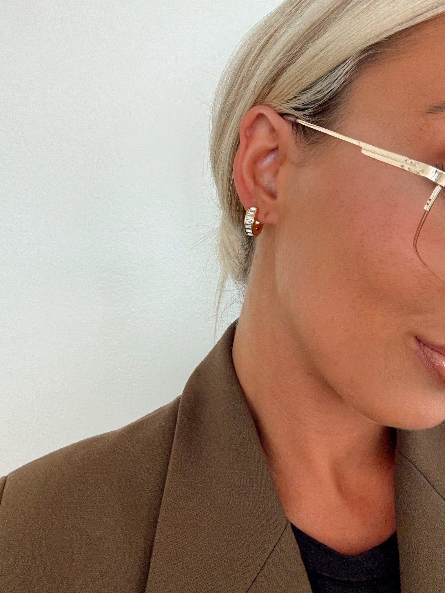 Close-up of a person wearing gold hoop earrings and glasses against a white background