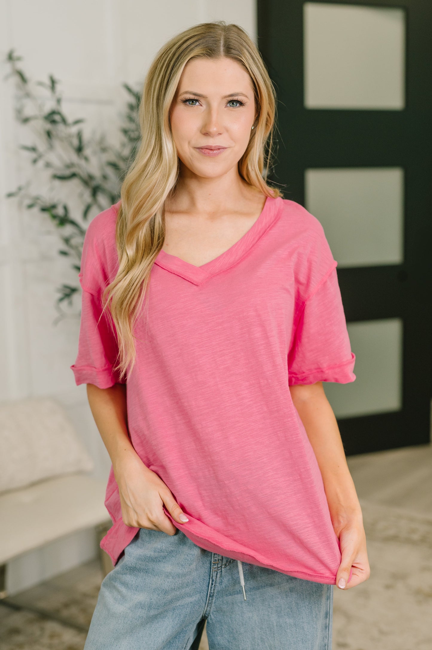 Woman wearing a pink top and blue jeans indoors with a blurred background