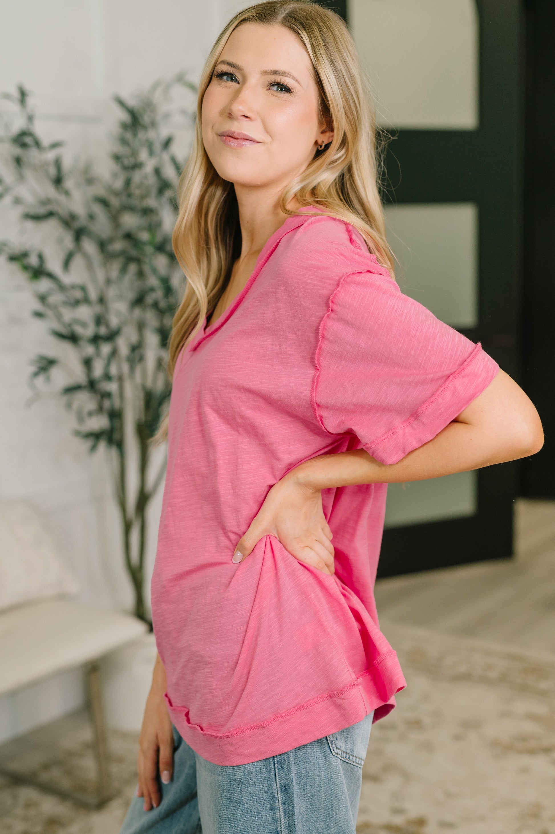 Woman wearing a pink top and blue jeans standing indoors.