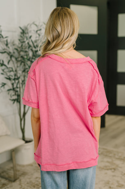 Person wearing a pink shirt and blue jeans standing in a room with a plant and a black and white abstract painting.