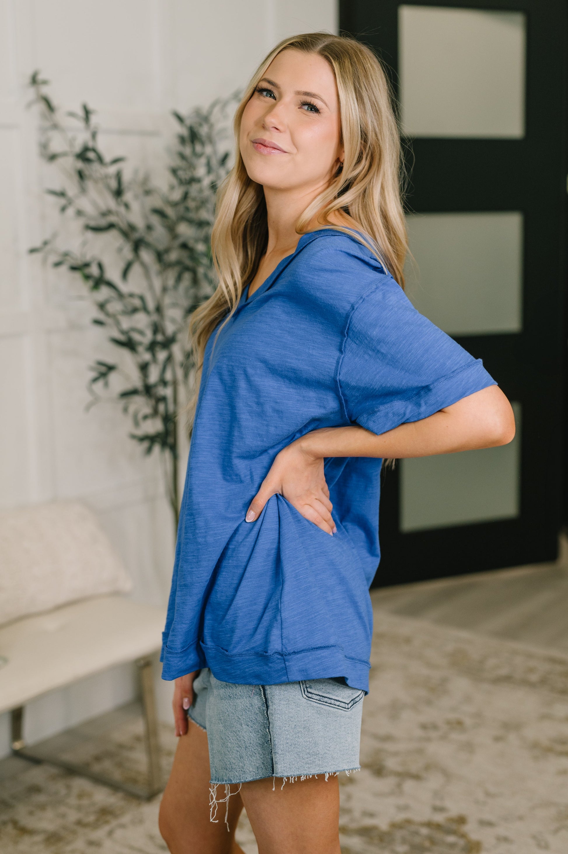 Woman wearing a blue top and denim shorts standing indoors.