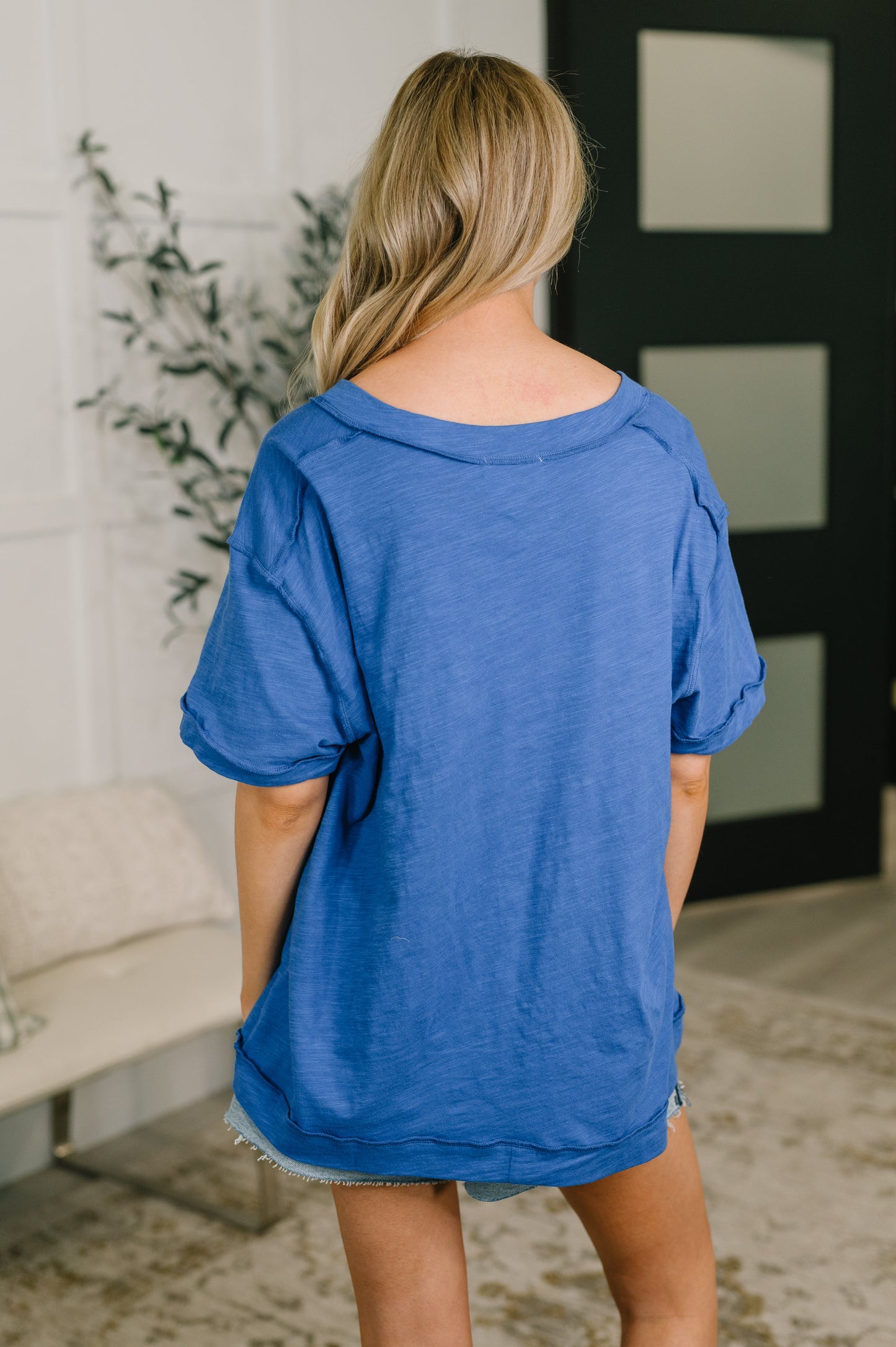 Woman wearing a blue oversized t-shirt in a room with a plant and sofa.