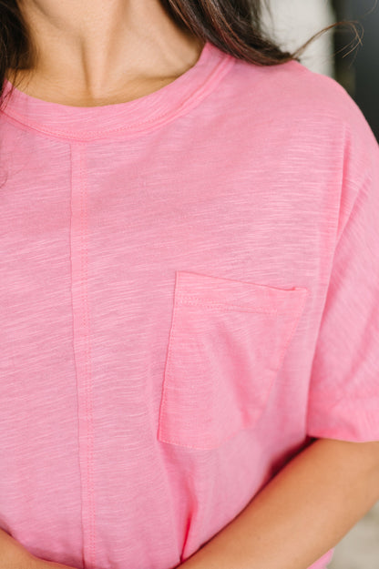 A close-up of a person wearing a pink short-sleeve crewneck t-shirt with a chest pocket, showing the fabric texture and fit.