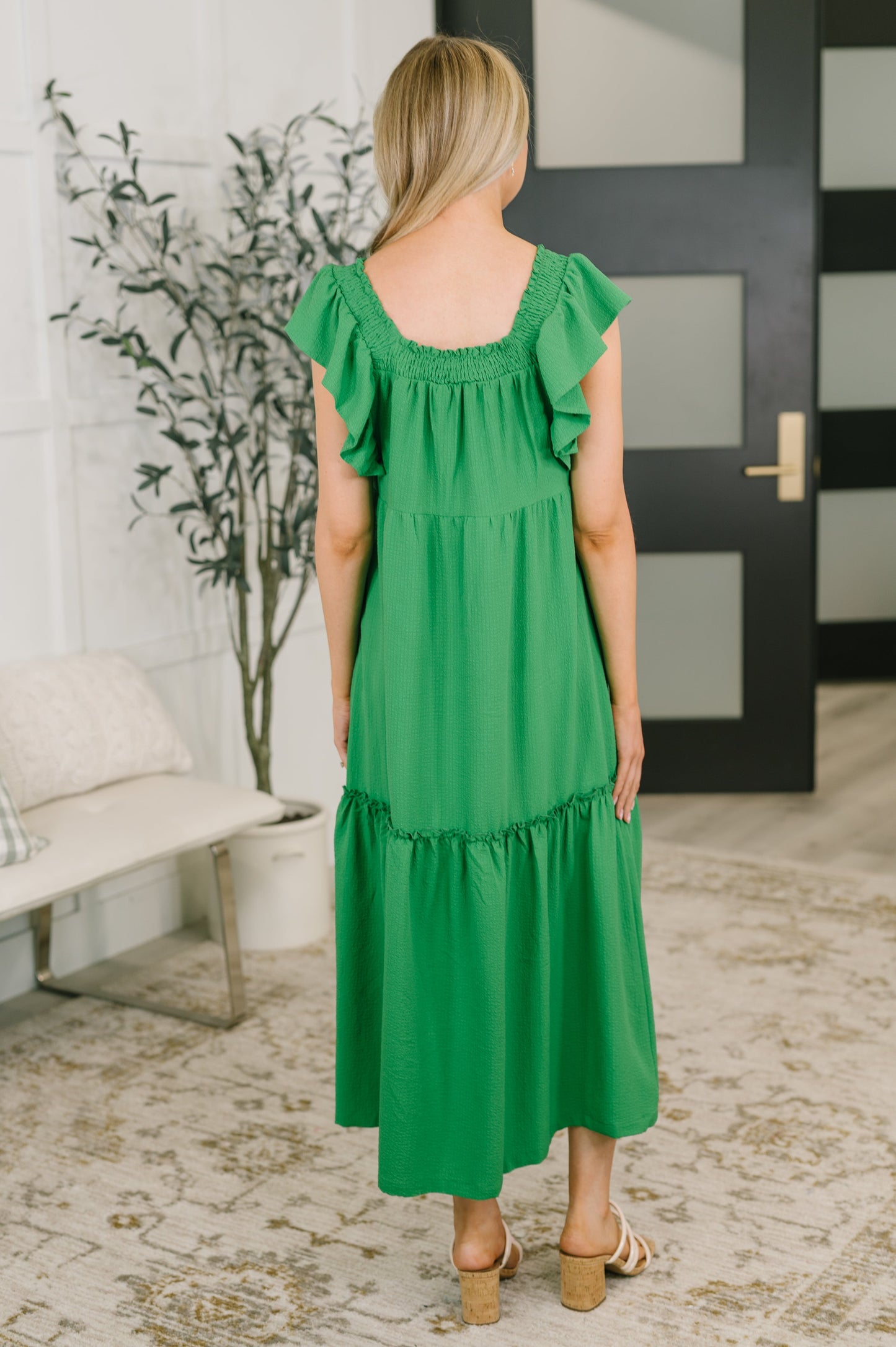 Woman wearing a green dress in an indoor setting with a plant and door in the background.