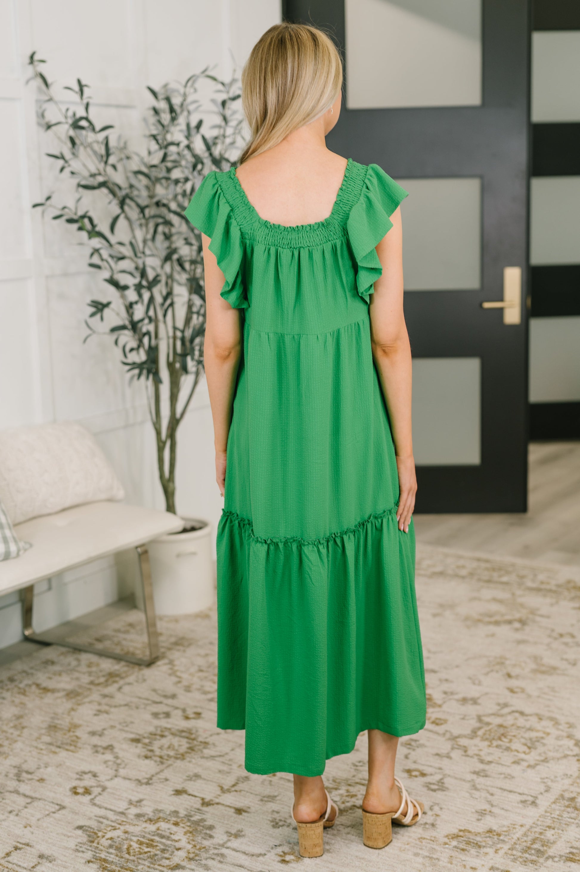 Woman wearing a green dress in an indoor setting with a plant and door in the background.