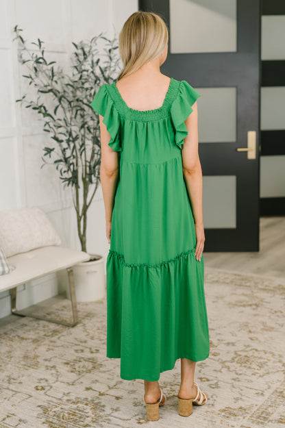 Woman wearing a green dress in an indoor setting with a plant and door in the background.