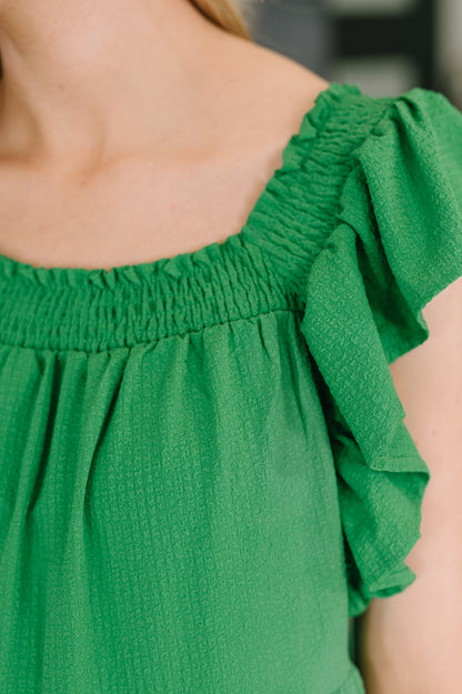 Green top with ruffled shoulders worn by a person, blurred background
