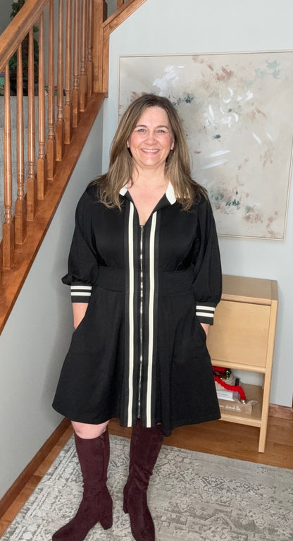 Woman in a black dress with white accents standing in a home setting.