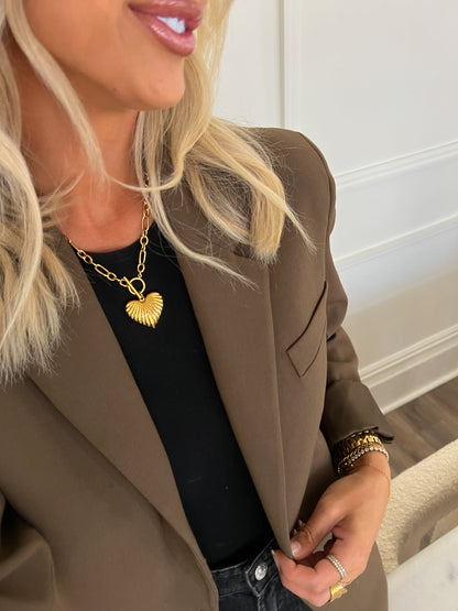 Woman wearing a brown blazer with a gold necklace and bracelet indoors.