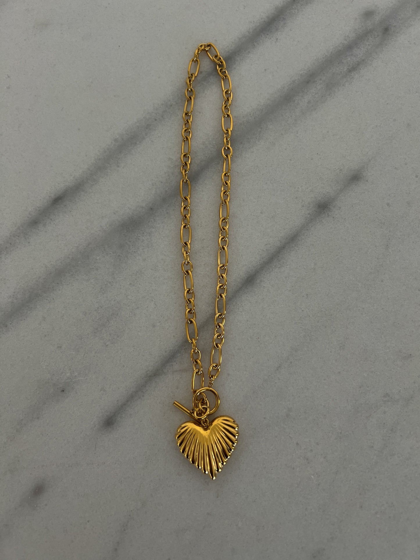 Gold chain necklace with a heart pendant on a gray surface