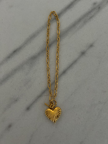 Gold chain necklace with a heart pendant on a gray surface