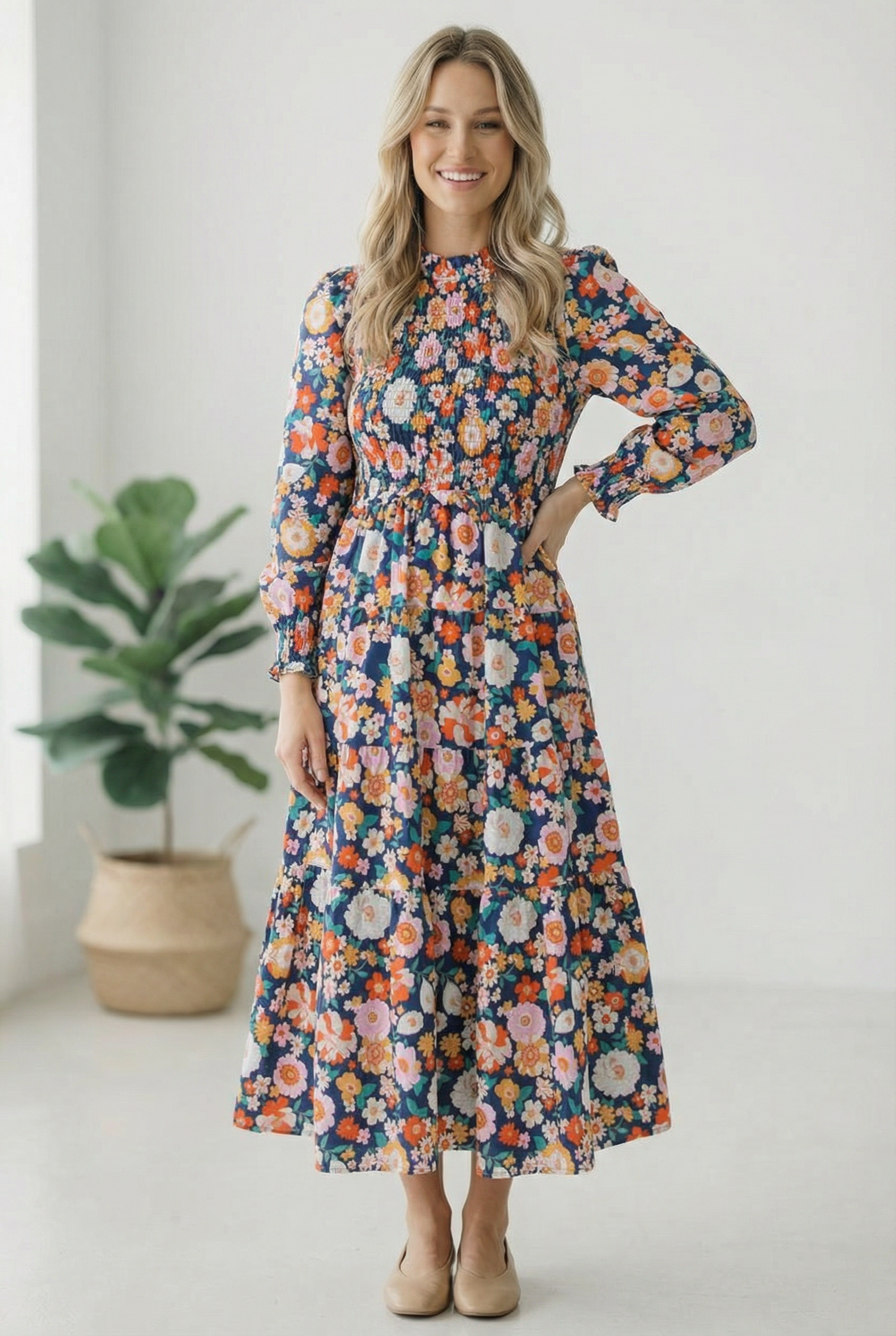Woman wearing a floral dress standing in a minimalistic room with a plant.