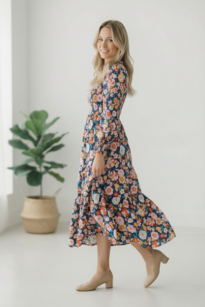 Woman wearing a floral dress standing in a minimalistic room with a plant.