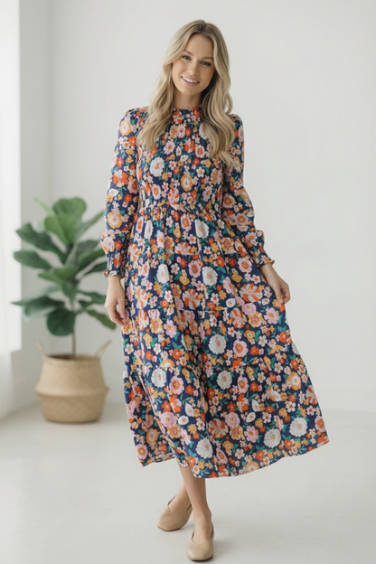 Woman wearing a floral dress standing in a room with a plant.