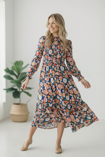 Woman wearing a floral dress standing indoors with a plant in the background