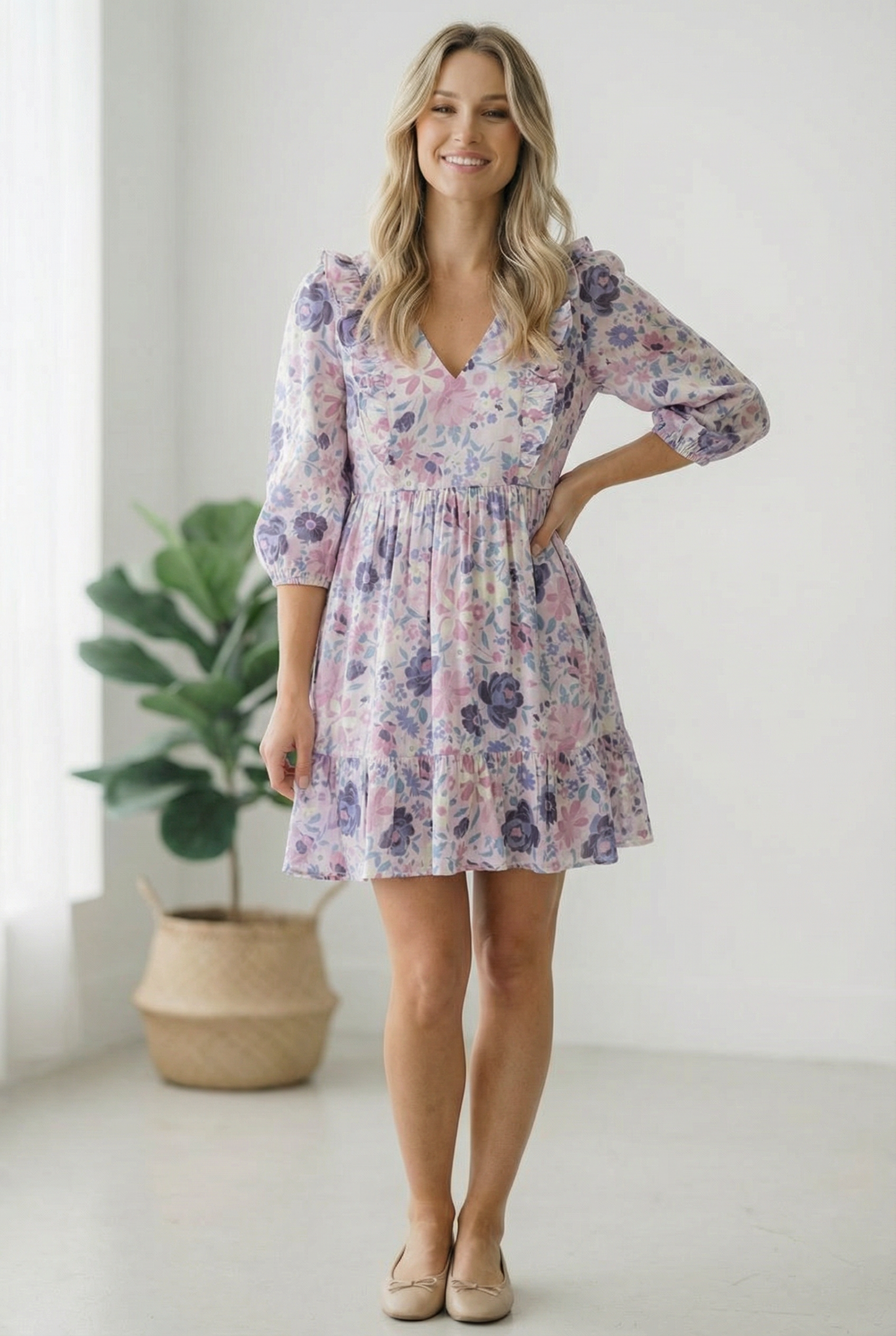 Woman wearing a floral dress standing in a bright room with a plant in the background