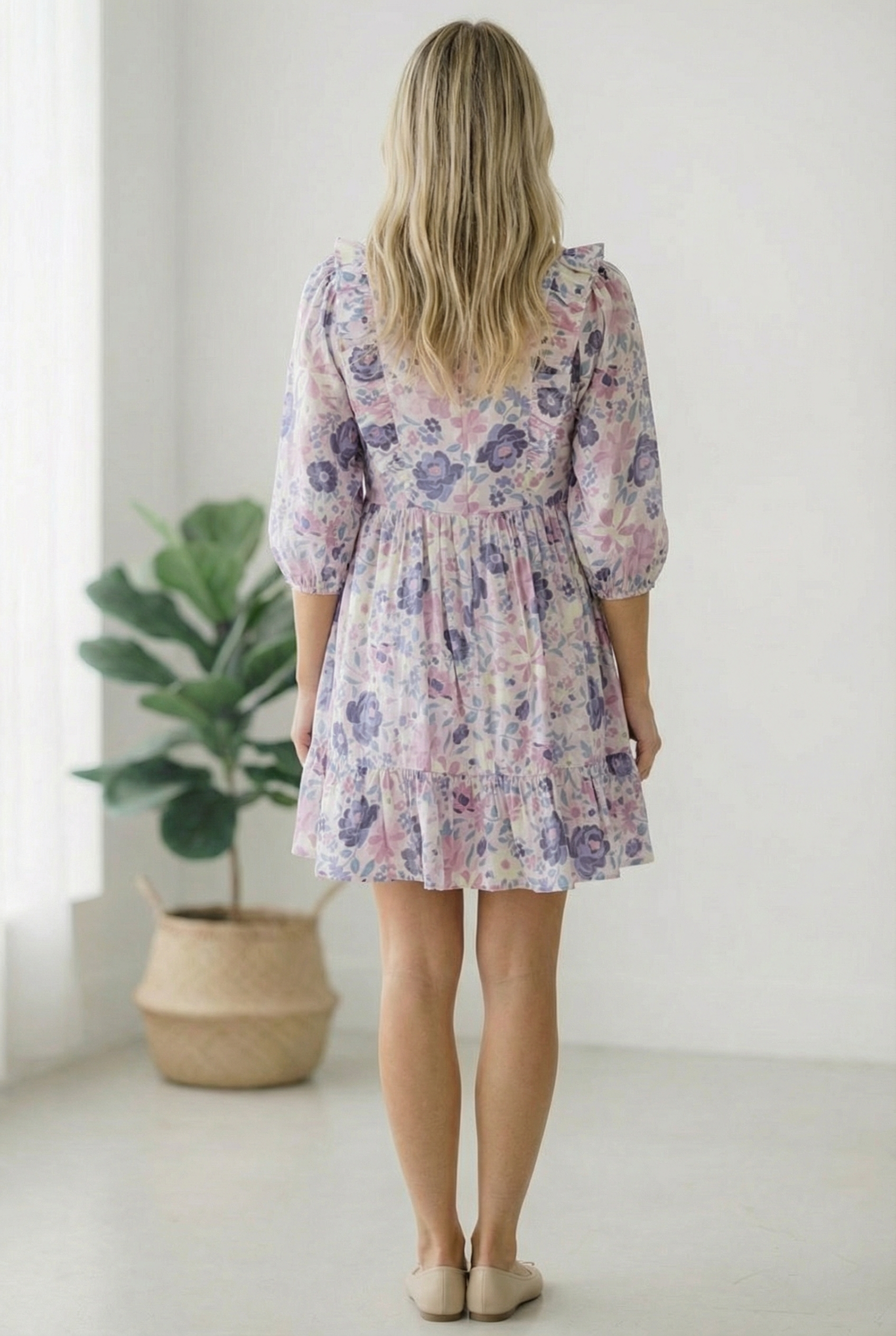 Woman wearing a floral dress standing in a minimalistic room with a plant.