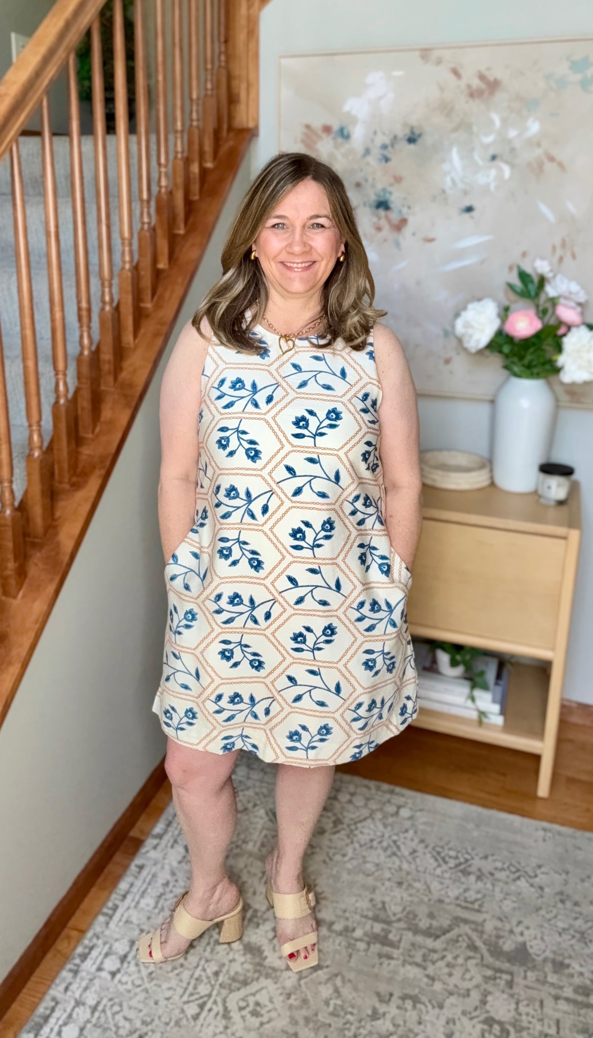 Woman wearing a sleeveless dress with a floral pattern in a home setting.