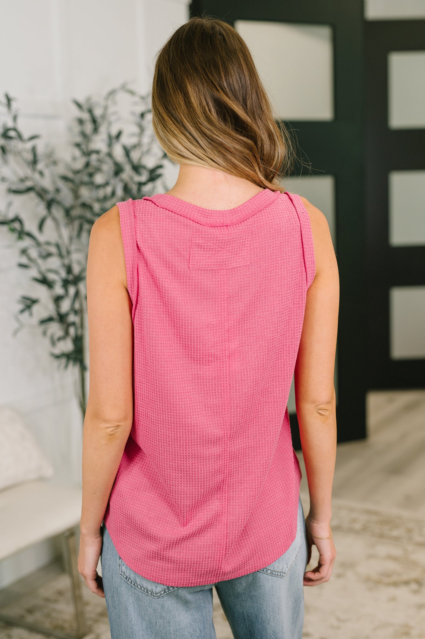 Person wearing a pink sleeveless top and blue jeans standing indoors.