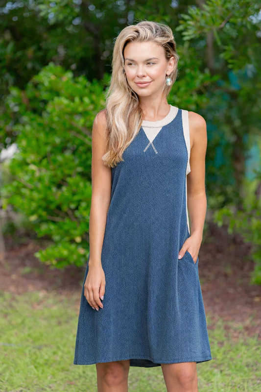 Woman wearing a blue dress standing outdoors with greenery in the background