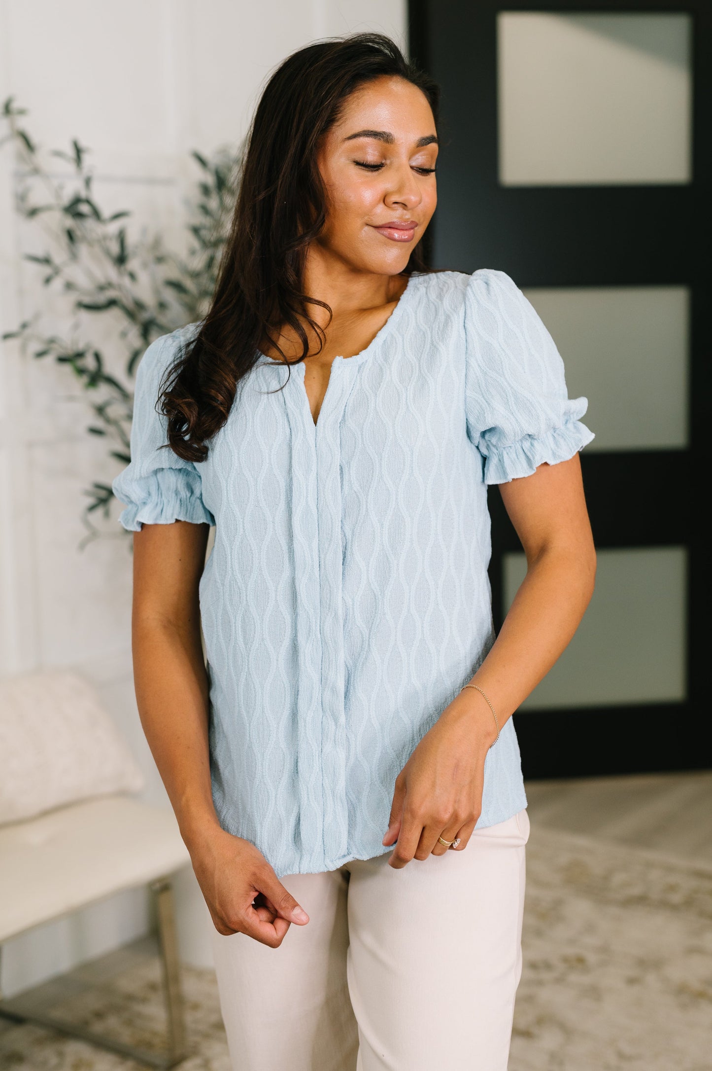 Woman wearing a light blue blouse with ruffled sleeves in an indoor setting.