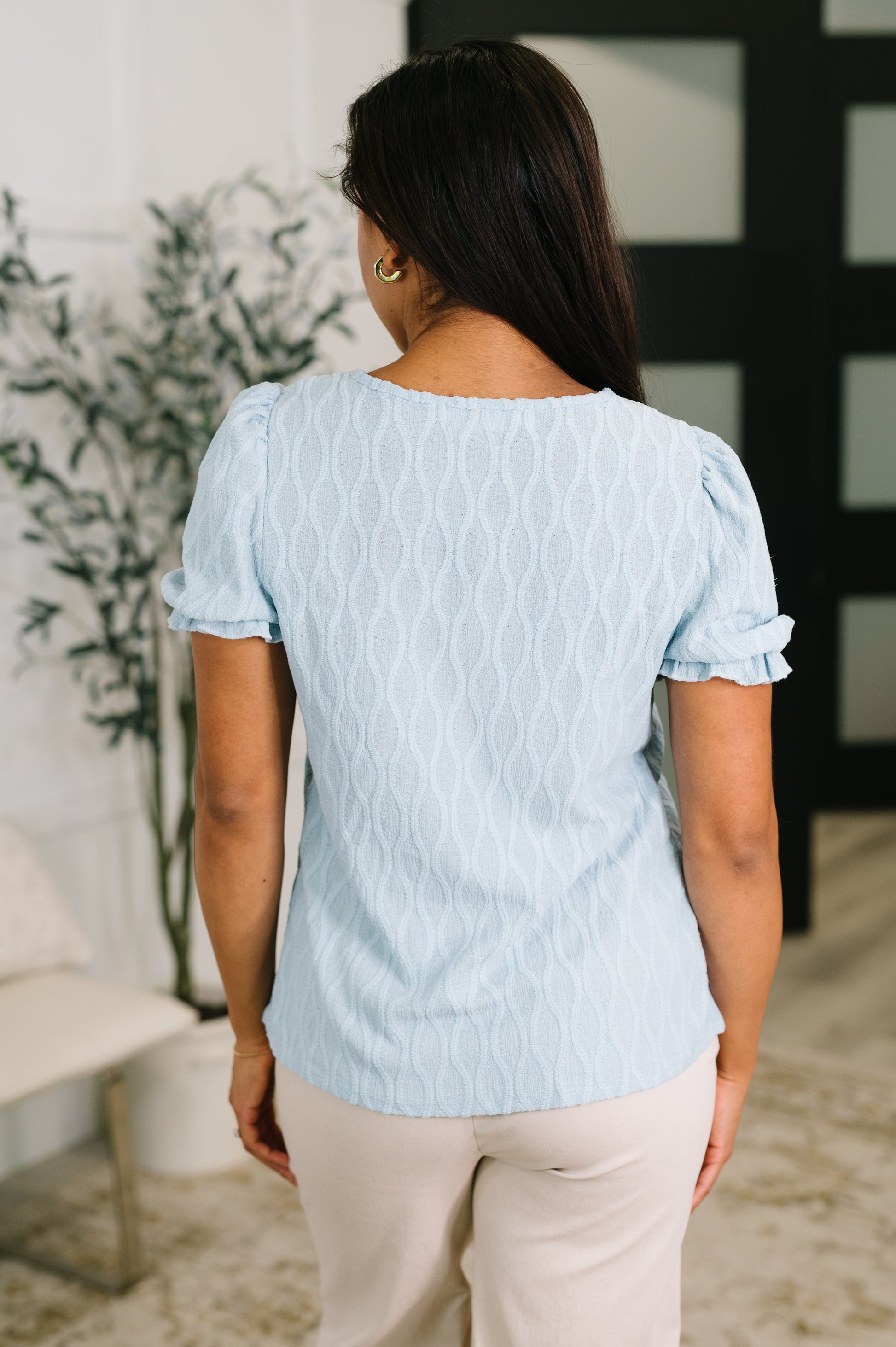 Woman wearing a light blue textured blouse in an indoor setting