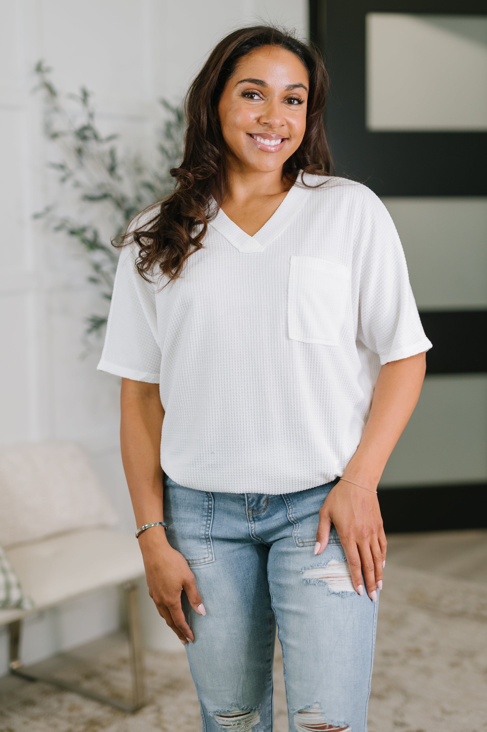 Woman wearing a white ribbed sweater and light blue jeans indoors.