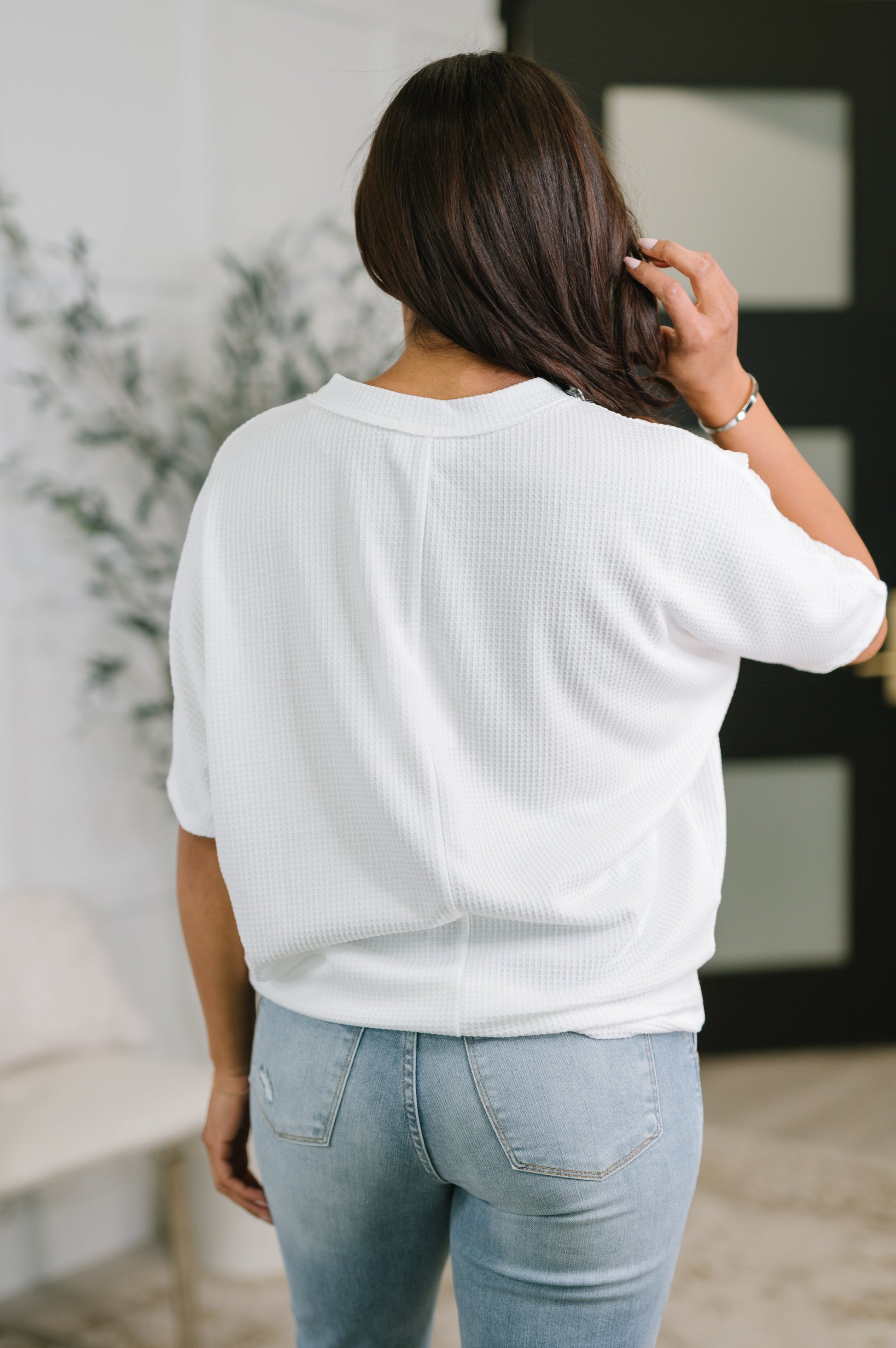 Person wearing a white sweater and light blue jeans indoors.