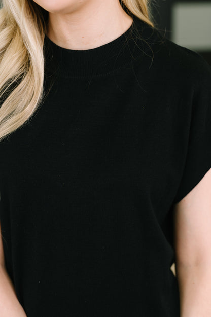 Close-up of a person wearing a plain black short-sleeve crew-neck top, with blonde hair visible at the left edge.